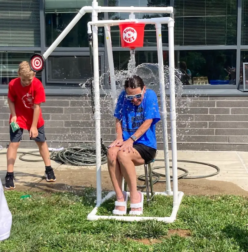 A staff member sitting on the dunk tank seat as students line up to throw